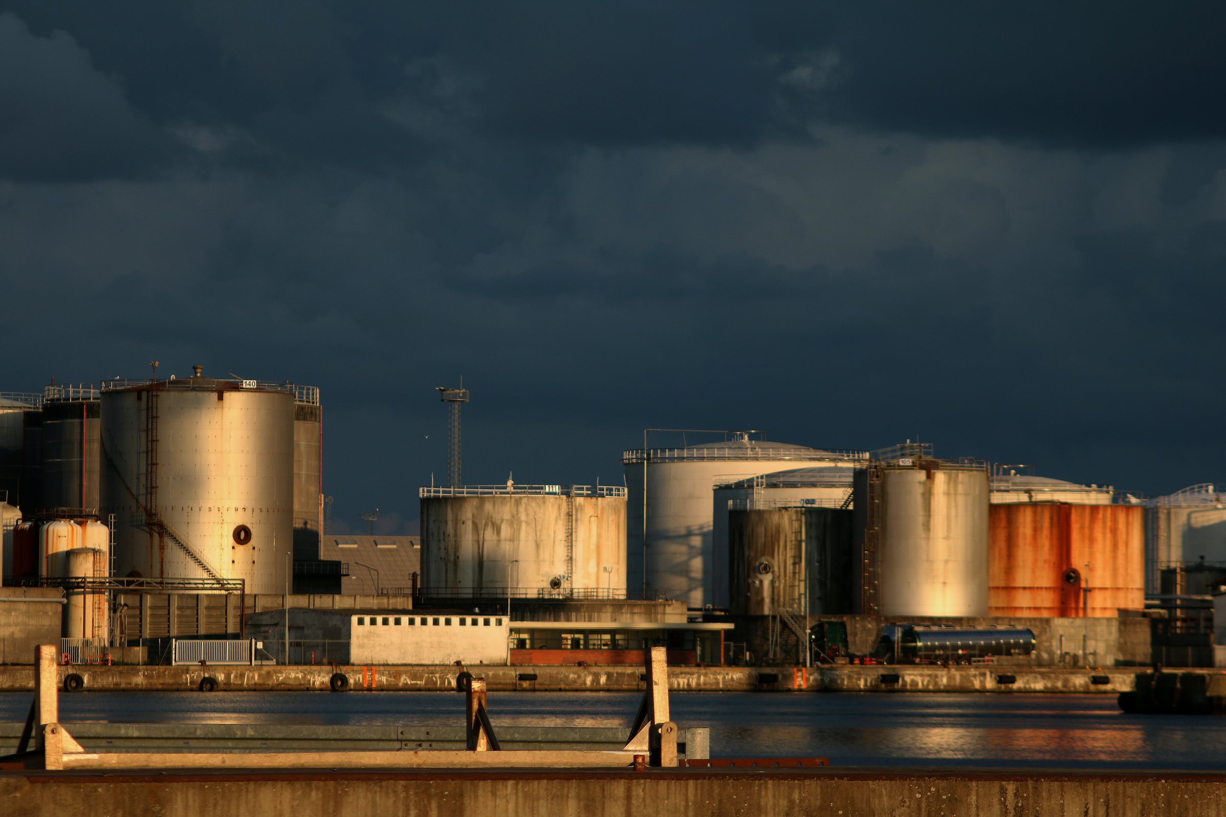 Storage tanks and process buildings at an industrial waterfront site in evening light