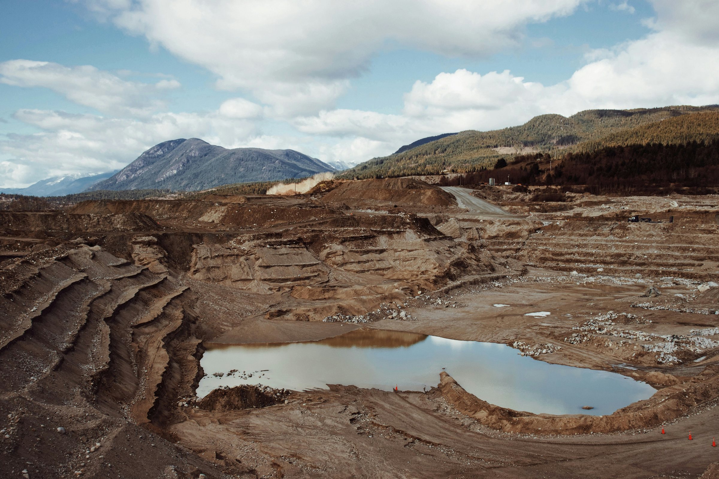 Terraced open-pit mine with a pool of water in the foreground and mountains beyond