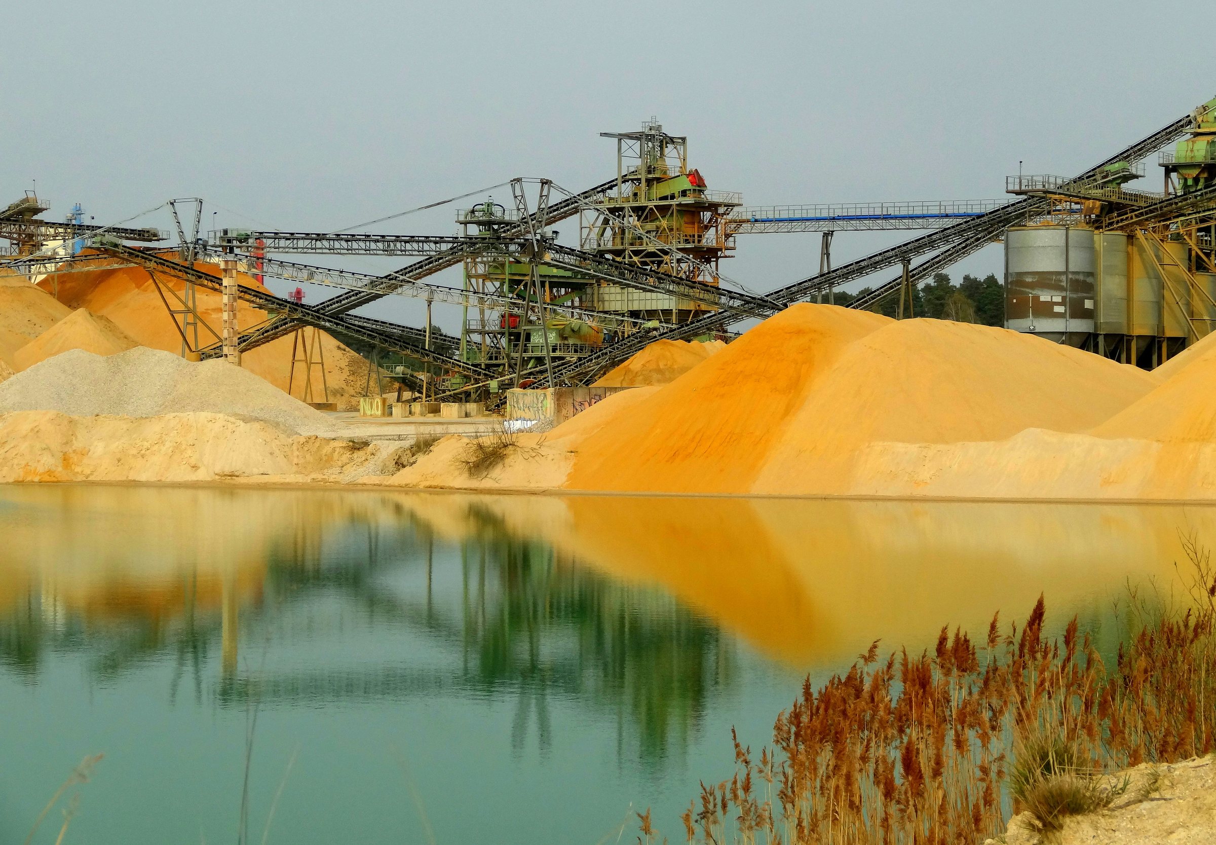 Mineral processing plant with conveyors and sand stockpiles beside a settling pond