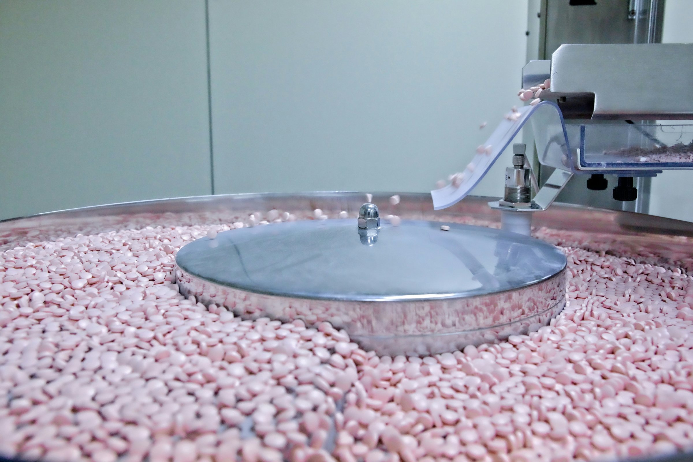 Tablets on a stainless-steel rotary feeder in a pharmaceutical production room